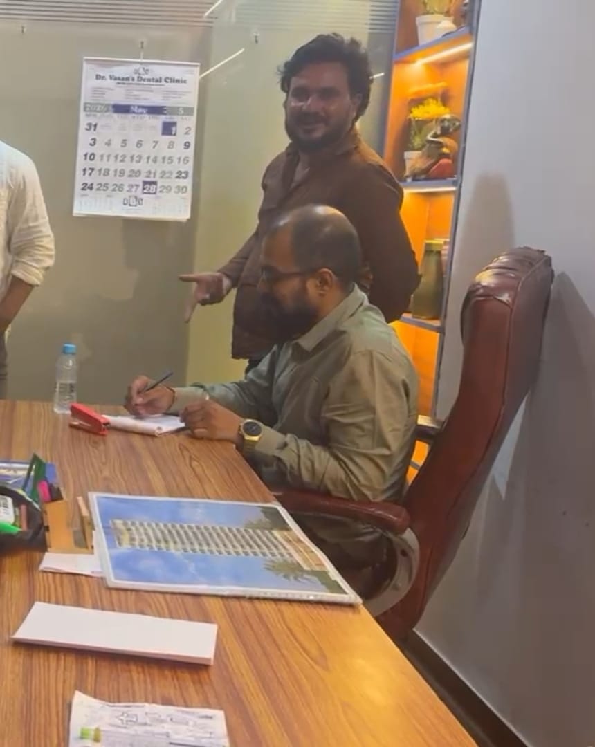 Man customers identify as Vinodkumar Prajapati (Vicky) standing in Future Wings International office, with Sumit Choudhari seated at the desk